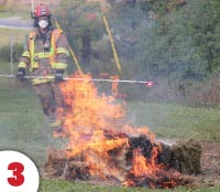 hay bale on fire with fireman standing beside